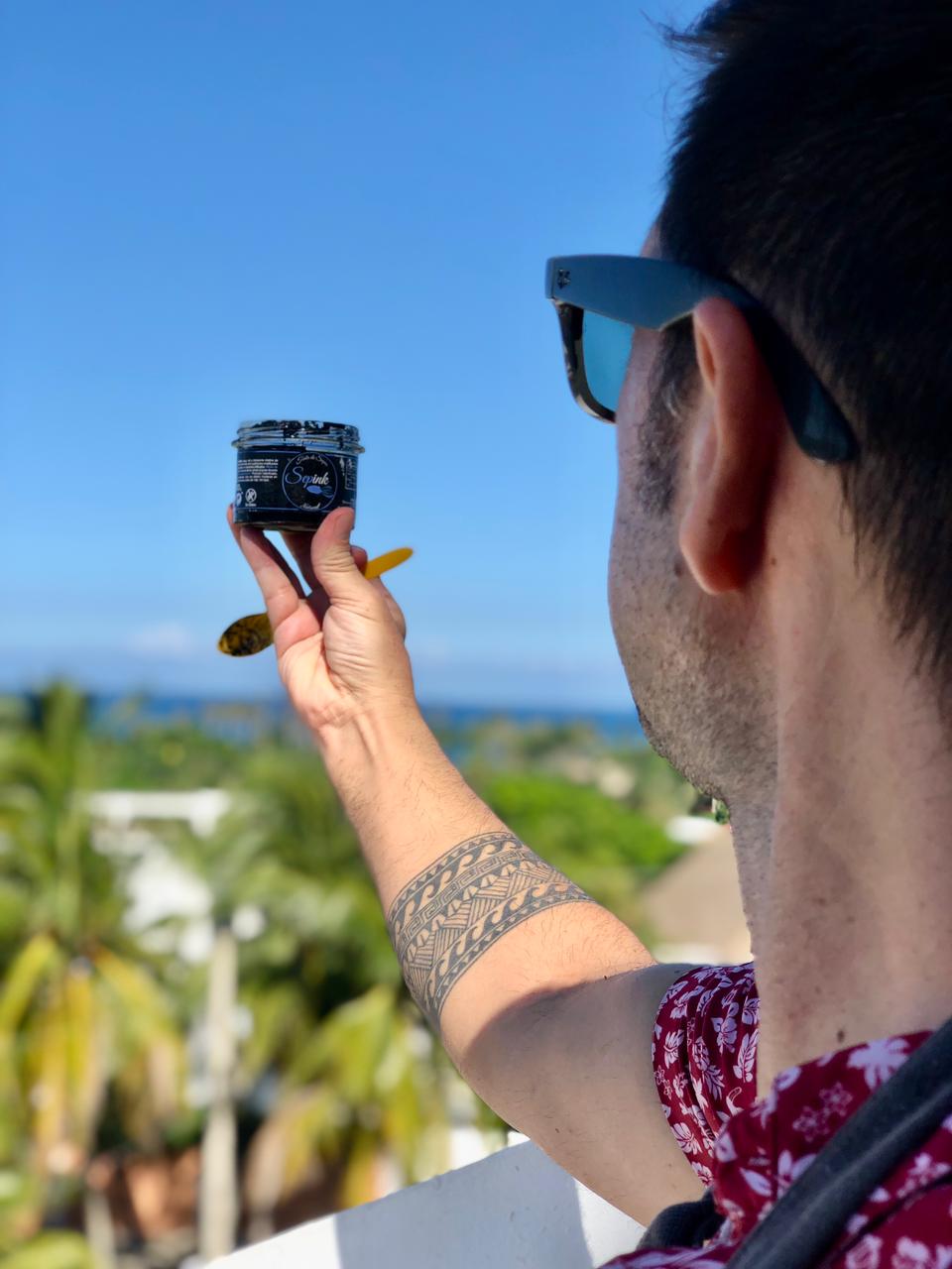 Mano sujetando bote de tinta de calamar con el mar de fondo