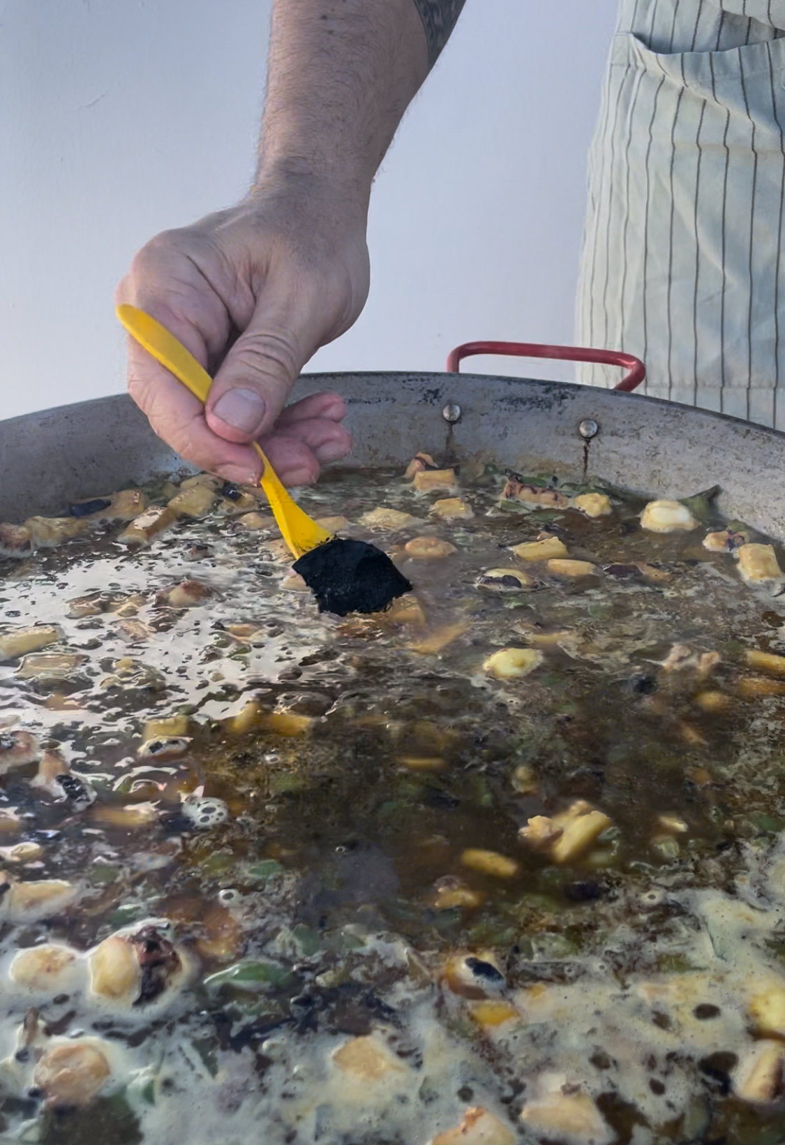 Mano del cocinero virtiendo tinta en el paellero